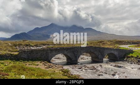 Alte alte Backsteinbrücke über den Fluss in Sligachan, Isle of Skye, Schottland mit Schafen auf Brücke und schottische Landschaft, Vegetation, Hügel und Berge Stockfoto