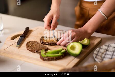 Frau macht Avocado Erdnussbutter Toast für ein gesundes Frühstück zu Hause Stockfoto