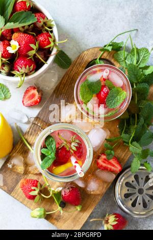 Sommerdrink erfrischend. Limonade mit frischen Erdbeeren, Eis und Zitronen auf einer leichten Steinplatte. Draufsicht flach legen Hintergrund. Stockfoto