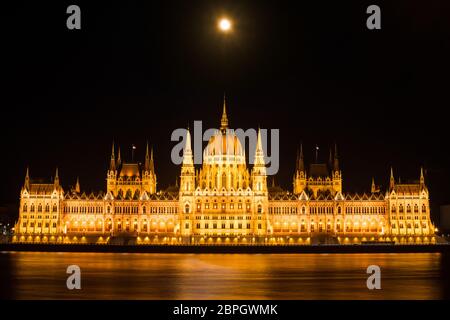 Wahrzeichen des ungarischen parlamentsgebäudes in Budapest bei Nacht mit Mond auf dunklem schwarzen Himmel. Stockfoto