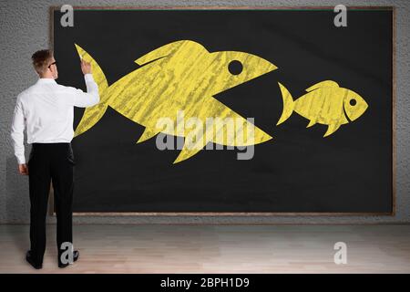 Rückansicht eines Geschäftsmannes Zeichnung Skizze der grosse Fische fressen Kleine Fische auf der Tafel Stockfoto