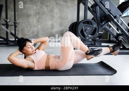 Junge hübsche Frau im mittleren Alter, gut gebauter Körperbau, übt Übungen an der Presse aus. Stockfoto