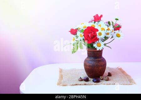 Blumenstrauß aus den weißen Gänseblümchen und rote Rosen in Lehmtöpfen ist auf Entlassung. Blumen im Topf auf lila Hintergrund. Gänseblümchen und rote Rosen in der Vase auf dem Tisch Stockfoto