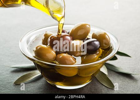 Bio Olivenöl. Flasche kaltgepresstes Öl in das Glasgefäß mit Oliven gießen Stockfoto