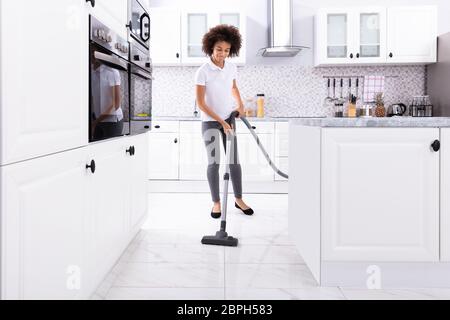 Nahaufnahme einer jungen Frau Reinigung der Weißen Küchenboden mit Staubsauger absaugen Stockfoto