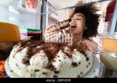 Junge Frau essen Kuchen aus dem Kühlschrank. Stockfoto