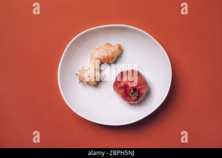 Reifer Granatapfel und Ingwerwurzel auf einem Teller auf orange-rotem Hintergrund. Stockfoto