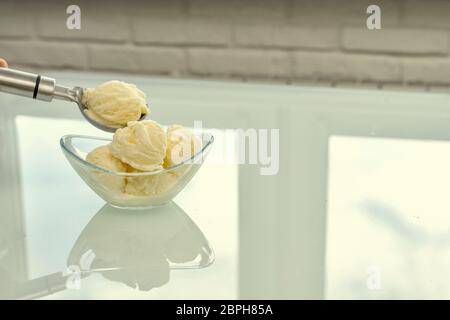 Eine Schüssel mit Vanille-Eis steht auf einem reflektierenden hellen Tisch. Mit einem Metalllöffel Bericht ein weiterer 1 Ball Stockfoto