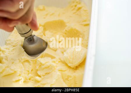 Vanilleeis. Ein Eislöffel nimmt ein wenig aus der Verpackung. Der Eisball. Platz für Text. Stockfoto