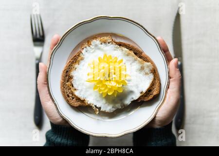 Konzeptionelles Bild des Frühstücks mit Spiegelei Toast. Gelbe Chrysanthemum Blume statt Dotter serviert auf einem weißen Teller Stockfoto