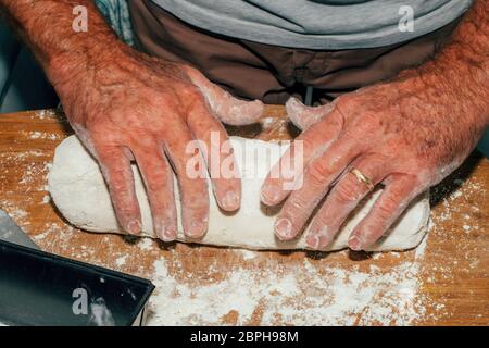 Nahaufnahme der Hände des Mannes, der den Brotteig auf einem Schneidebrett knetet. Stockfoto