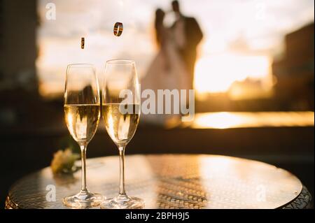 Zwei Gläser Champagner stehen auf einem Tisch stehen auf einem Tisch. Ein liebevolles Paar von Brautpaar steht im Hintergrund. Stockfoto