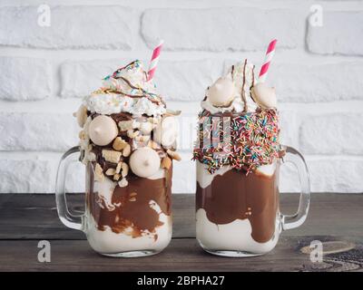 Nahaufnahme von zwei Freakshake im Einmachglas auf braunen Tisch. Ausgeflippt Milchshake mit Schokolade, Keks Kekse und Zucker bestreuen. Trendige Lebensmittel conce Stockfoto