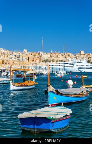 Zu den traditionellen maltesischen Boote mit superyachten im Hintergrund mit Valletta, die im Hintergrund von Senglea, Malta gesehen sichtbar Stockfoto