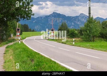 Landschaftsansicht einer Landstraße Kurve mit offenen begrenzten Bahnübergang, St. Andrew's Cross und Straßenschild gegen alpine Berglandschaft in der Summe Stockfoto