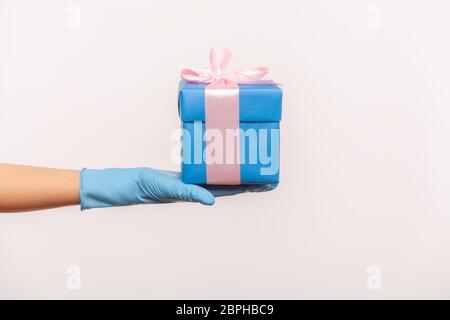 Profil Seitenansicht Nahaufnahme der menschlichen Hand in blauen chirurgischen Handschuhe mit blauen Geschenk-Box. Teilen, geben oder Lieferung Konzept. Indoor, Studio erschossen, isola Stockfoto