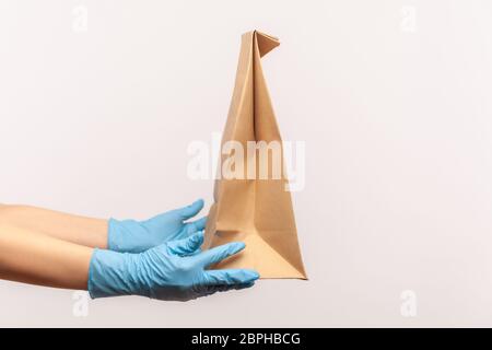 Profil Seitenansicht Nahaufnahme der menschlichen Hand in blauen chirurgischen Handschuhen halten und Handwerk Papierpaket mit Lebensmitteln. Sichere Lebensmittel-Delivery-Konzept. Indoor, Studio s Stockfoto