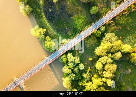 Luftaufnahme einer schmalen Straßenbrücke, die sich über einen schlammigen, breiten Fluss in grüner ländlicher Umgebung erstreckt. Stockfoto