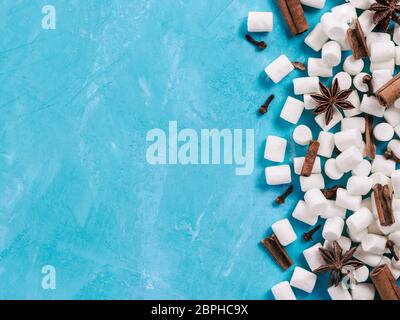 Marshmallows und Winter Gewürze auf blauem Hintergrund mit Copyspace. Flach oder der Ansicht von oben. Hintergrund der bunten mini Marshmallows, Zimt, Nelken und Stockfoto