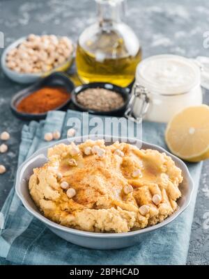 Hausgemachte Hummus mit Olivenöl in grau Schüssel und Zutaten. Traditionelle orientalische Vorspeise Hummus auf grauem Hintergrund - gesunde vegane Einfügen snac Stockfoto