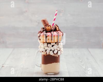 Schokolade Donuts und extreme Milchshake mit Marshmallow und andere Süßigkeiten in Mason jar auf grau Holz- Hintergrund. Crazy freakshake auf grau Holztisch Stockfoto