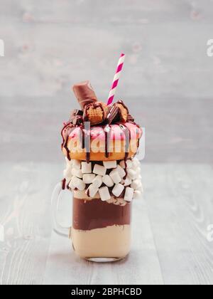 Schokolade Donuts und extreme Milchshake mit Marshmallow und andere Süßigkeiten in Mason jar auf grau Holz- Hintergrund. Crazy freakshake auf grau Holztisch Stockfoto