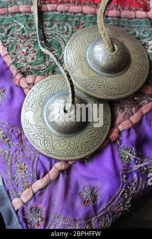 Tingsha (Ting-Sha), tibetische Meditationsglocken in Nahaufnahme, die auf einem bunten indischen Kissen liegen. Selektiver Fokus, Copyspace darunter. Stockfoto