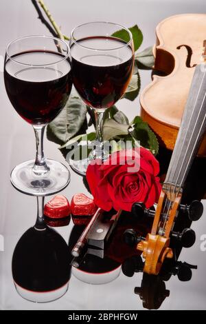 Geige (Geige), rote Herzen, zwei Gläser Wein und rote Rose auf schwarzem Hintergrund. Saiteninstrument. Valentinstag. Stockfoto