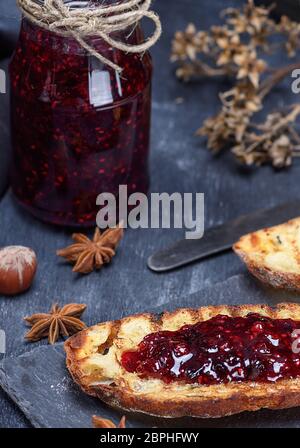 Himbeermarmelade mit einem Glas und Weißbrotscheiben auf schwarzem Hintergrund Stockfoto