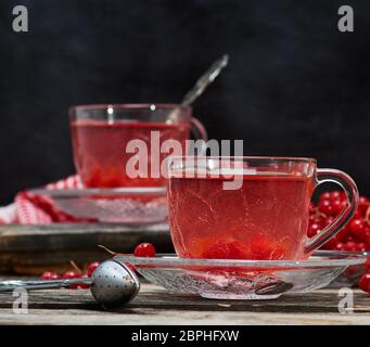 Viburnum heißen Tee in eine transparente Schale mit Griff und Untertasse auf einem grauen Holztisch Stockfoto