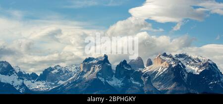 Sonnenschein auf den zerklüfteten Gipfeln von Cuernos del Paine, mit blauem Himmel und weißen Wolken über, nach einem Schneesturm, Torres del Paine, Patagonien, Chile Stockfoto