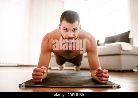 Nahaufnahme Porträt eines jungen Athleten. Ein junger Mann mit einer Sportfigur hat ein Training zu Hause. Die Brünette schaut auf die Kamera. Bleib zu Hause und behalte es Stockfoto