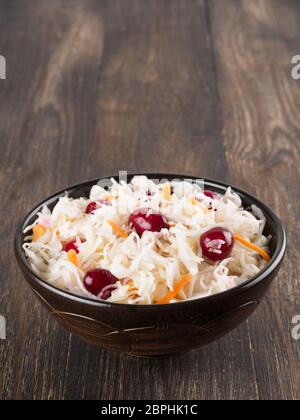 Traditionelle russische Vorspeise Sauerkraut mit Cranberry und Karotte in dunklen Handwerk Platte auf Braun rustikalen Holztisch. Fermentierter Kohl. Russische cuisin Stockfoto