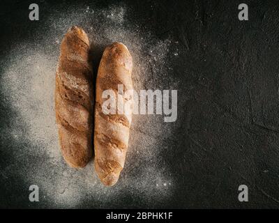 Zwei ganze hausgemachtes Brot Brot mit Buchweizen Buchweizen Mehl auf Schwarz strukturierten Hintergrund. Ansicht von oben oder flach-legen. Kopieren Sie Platz. Low Key Stockfoto