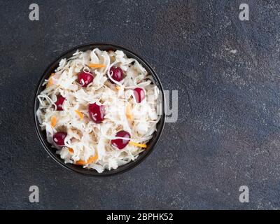 Traditionelle russische Vorspeise Sauerkraut mit Cranberry und Karotte in dunklen Schüssel auf schwarzem Zement Hintergrund. Fermentierter Kohl. Russische Küche und Rus Stockfoto