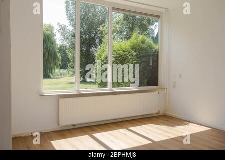 Leere weiße Zimmer mit Parkettboden Parkettboden, große Fenster und Wände und Sonnenlicht vom Fenster, mit einem schönen, grünen Wald Natur anzeigen modernes Haus Stockfoto