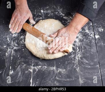 Koch in einem schwarze Tunika, rollt Teig für Pizza, Ansicht von oben Stockfoto