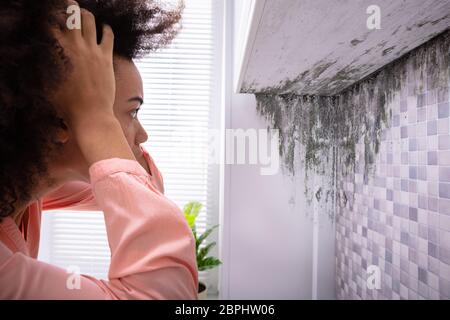 Seitenansicht eines Afrikanischen jungen Frau auf der Suche nach Schimmel auf Weiße Wand Stockfoto