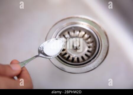 Eine Person, die Natron mit Löffel auf Abfluss im Waschbecken Stockfoto