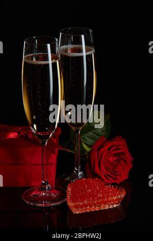 Zwei Weingläser Champagner, Geschenkbox, Rose und roter Kaviar auf Untertasse in Herzform auf schwarzem Hintergrund. Valentinstag Stockfoto