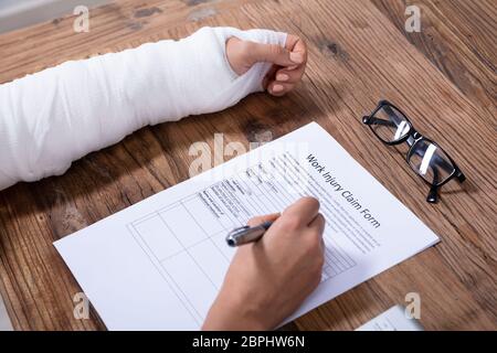 Nahaufnahme der Geschäftsfrau mit weißen Bandagen Hand Befüllen Arbeitsunfall Antragsformular auf hölzernen Schreibtisch Stockfoto