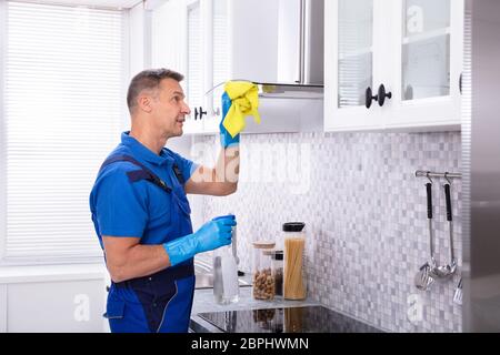 Reife männliche Hausmeister Reinigung Dunstabzugshaube mit Serviette und Spray Waschmittel in der Küche Stockfoto