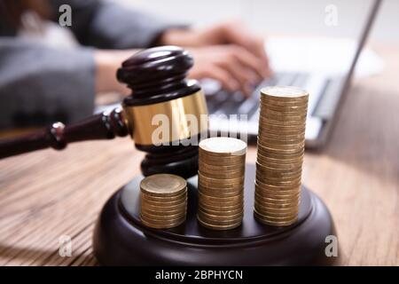 Nahaufnahme der zunehmenden Münzen und Hammer auf Hammer mit einer Person mit Laptop im Hintergrund Stockfoto