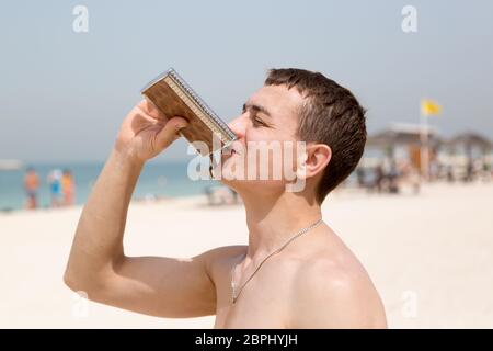 Ein 35-40-jähriger Mann trinkt starken Alkohol aus einer Eisenkollamne, während er sich am Stadtstrand entspannt. Stockfoto