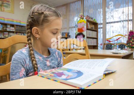 Ein Mädchen von zehn Jahre alt ist, ein Buch zu lesen in der Bibliothek Stockfoto