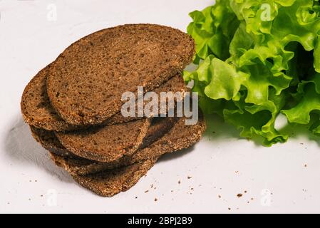 Grüne Blätter von frischem Salat und Brotscheiben auf weißem Hintergrund. Vegetarische Bio-Küche. Stockfoto