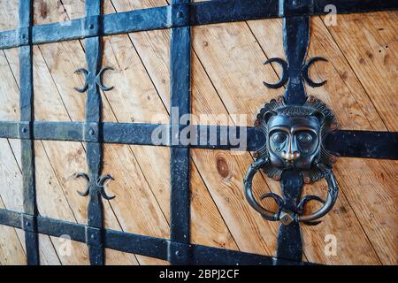Die hölzernen Türen mit dem schwarzen geschmiedeten Gitter mit dem Griff in Form des Löwenkopfes Stockfoto