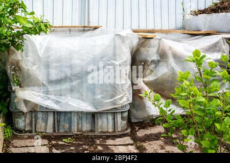 Kunststoffbehälter werden für Kompostierungsabfälle im Garten wiederverwendet. Frische Komposterde aus dem Kompostbehälter. Den Kompost von Regen und Wasserlog bedecken Stockfoto