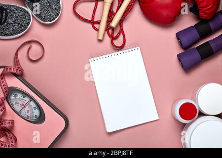 Weibliche Fitness Stillleben. Sporternährung (Ergänzungen), Sportaccessoires, ein leeres Blatt Notizbuch für die Planung der Ernährung und Schulungen auf rosa Rückenplatte Stockfoto