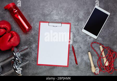 Fitness Stillleben. Sport-Zubehör: Hanteln, Seil, Boxhandschuhe, Computer-Tablet und Tablet mit leerem Blatt auf grauem Hintergrund. Draufsicht. Fitne Stockfoto